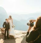 Bride and groom posing for photographer on mountain overlook.